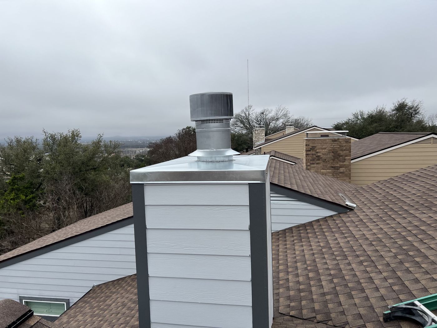 Round galvanized chimney cap on a chimney chase with gray trim