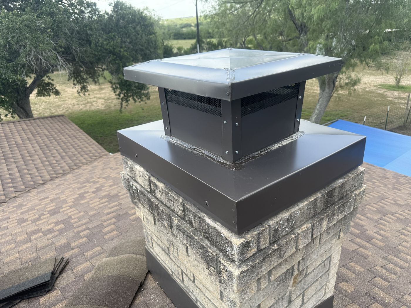 Bronze custom chimney cap with mesh sides on a stone chimney
