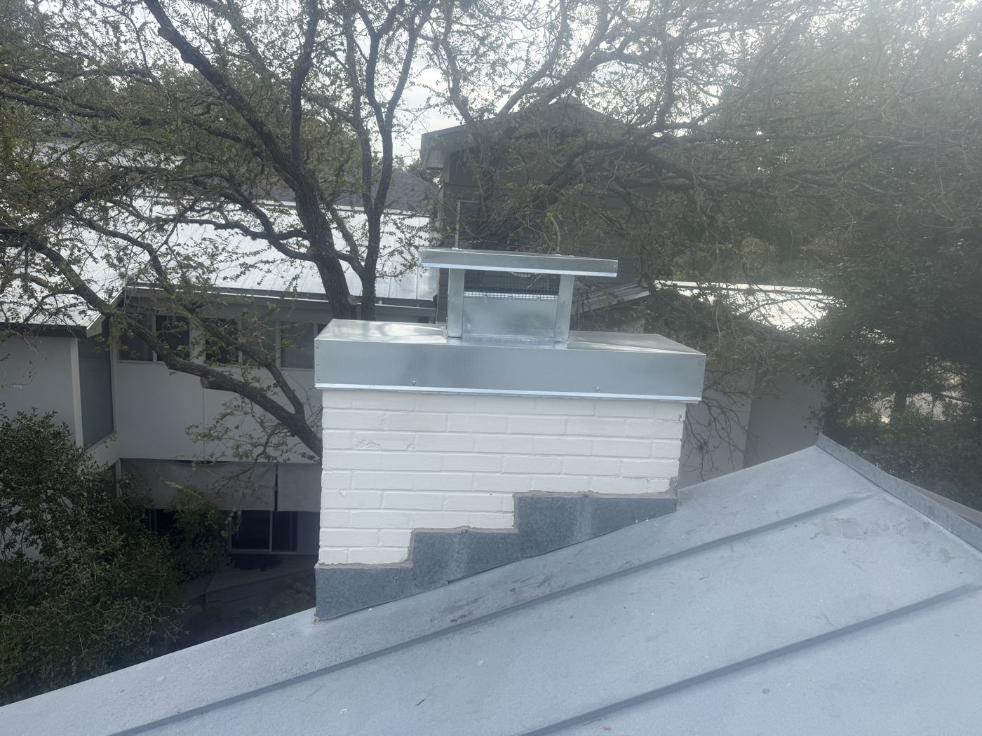 Wider view of a galvanized chimney cap on a painted white brick chimney