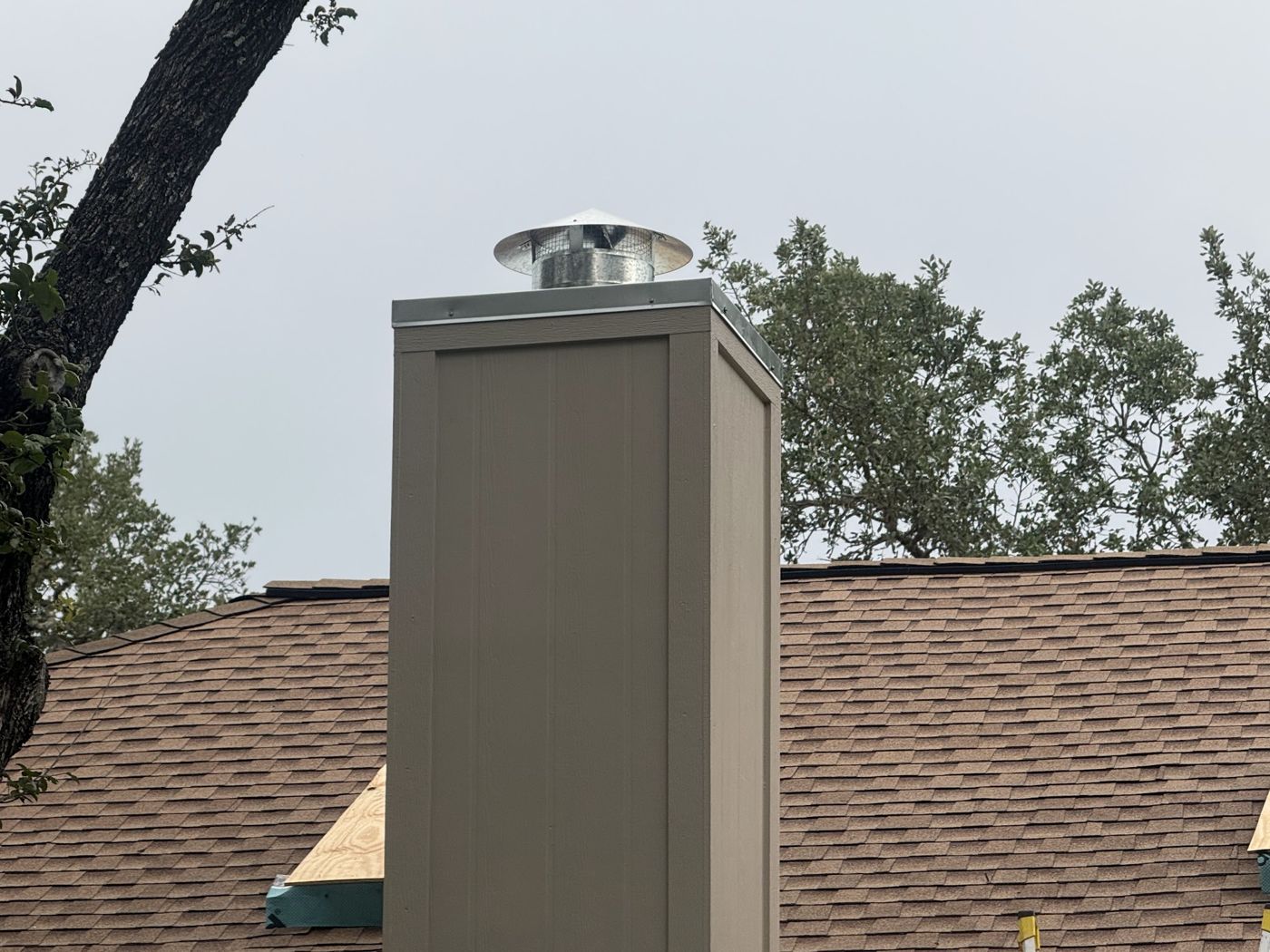 Custom galvanized chimney cap on a tan chimney above a shingle roof, San Antonio