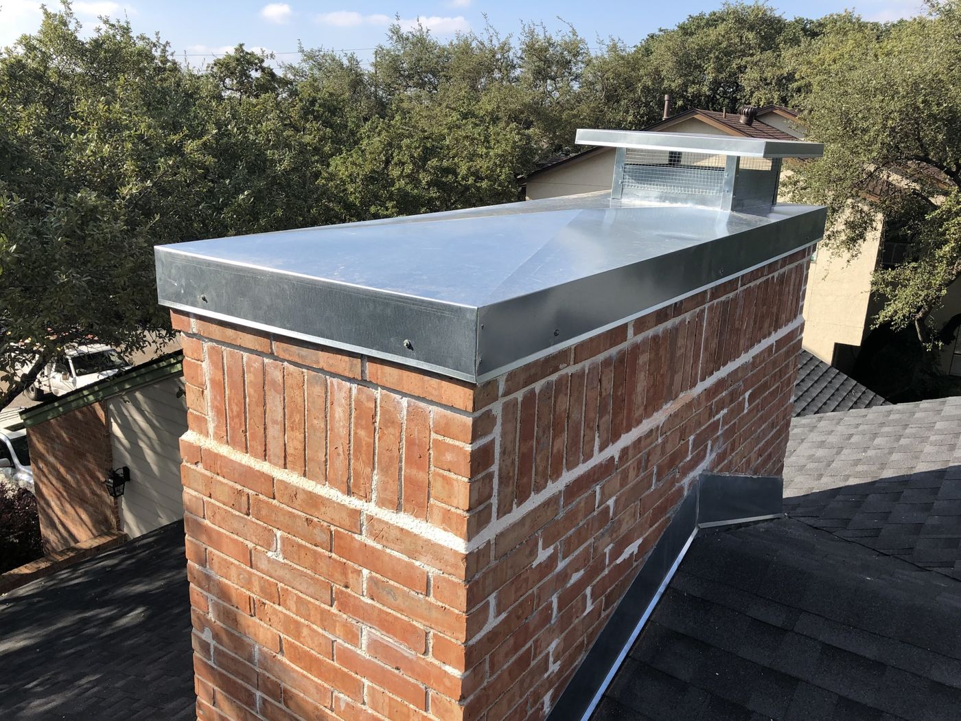 Long galvanized steel chimney cap with mesh screen on a red brick chimney, San Antonio