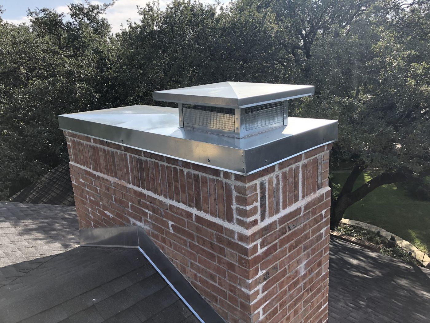 Galvanized pyramid-style chimney cap with mesh screen on a red brick chimney